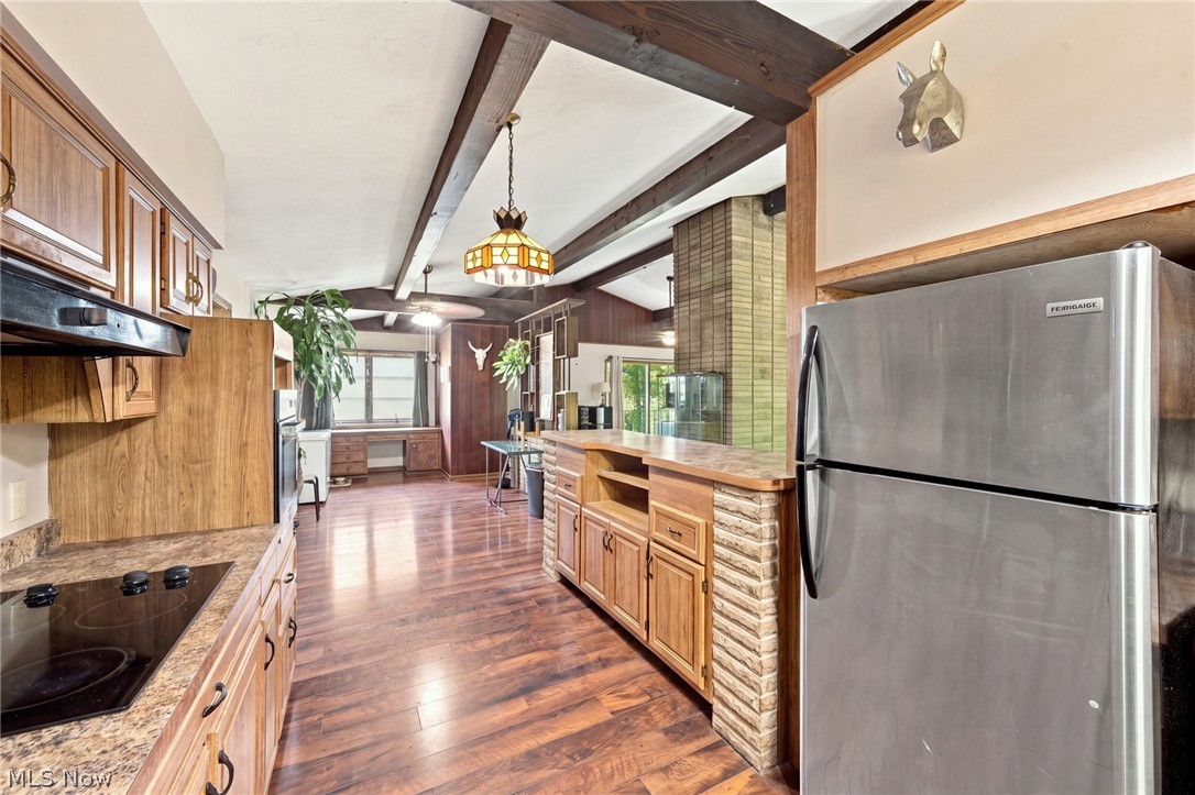 Kitchen with wood cabinetry, a stone-faced island, stainless steel refrigerator, and dark exposed ceiling beams.