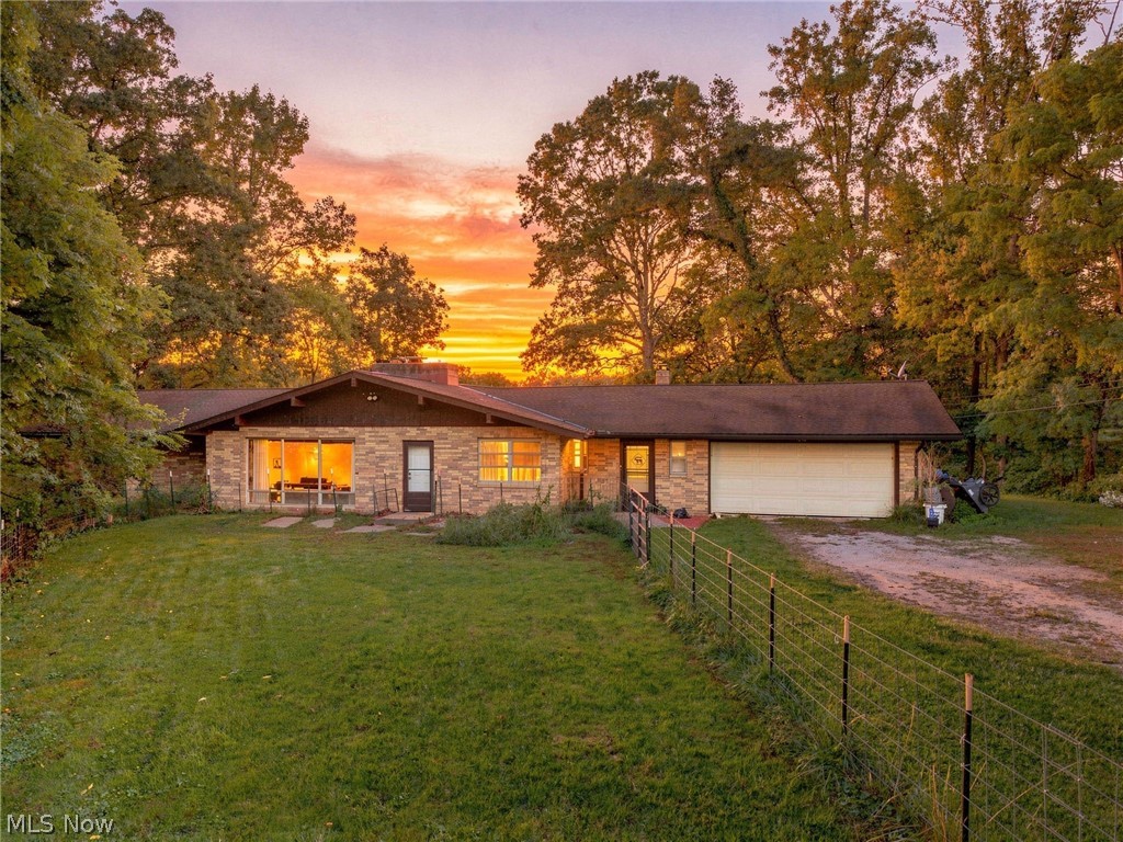 Brick ranch home with attached garage and fenced lawn beneath an orange sunset.