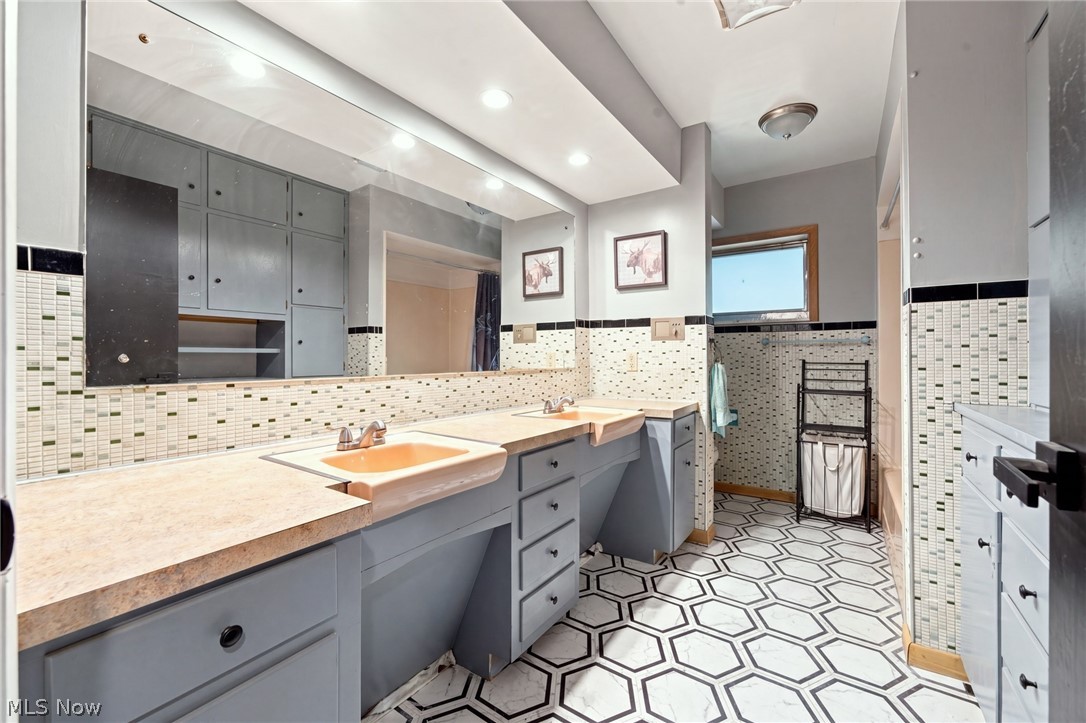 Bathroom with gray double vanity, mosaic tile walls, and a black-and-white geometric floor.