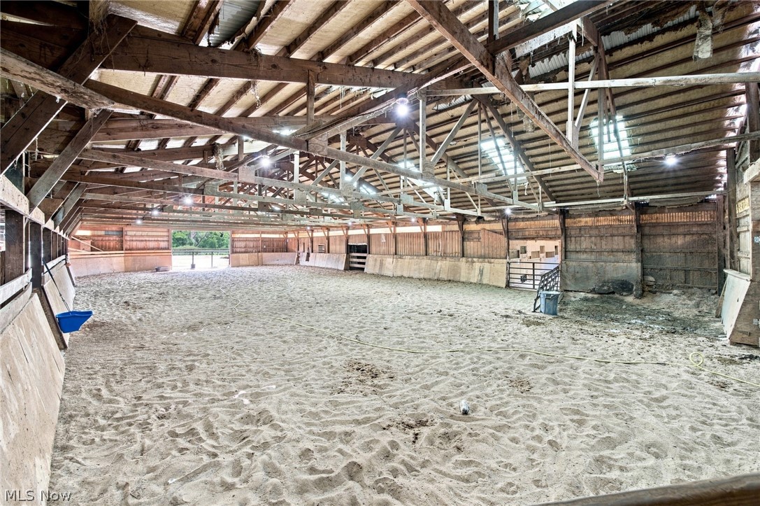 Indoor riding arena with a sand floor, exposed timber trusses, and gates along the sides.