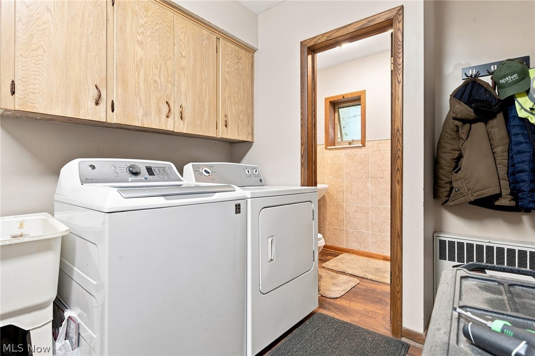 Laundry room with washer, dryer, light wood cabinets, and a doorway to a tiled bathroom.