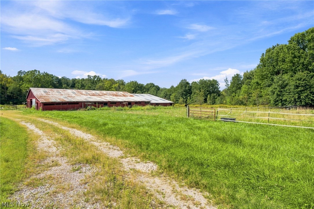 Red barn with a weathered metal roof beyond a grassy field and gravel track.