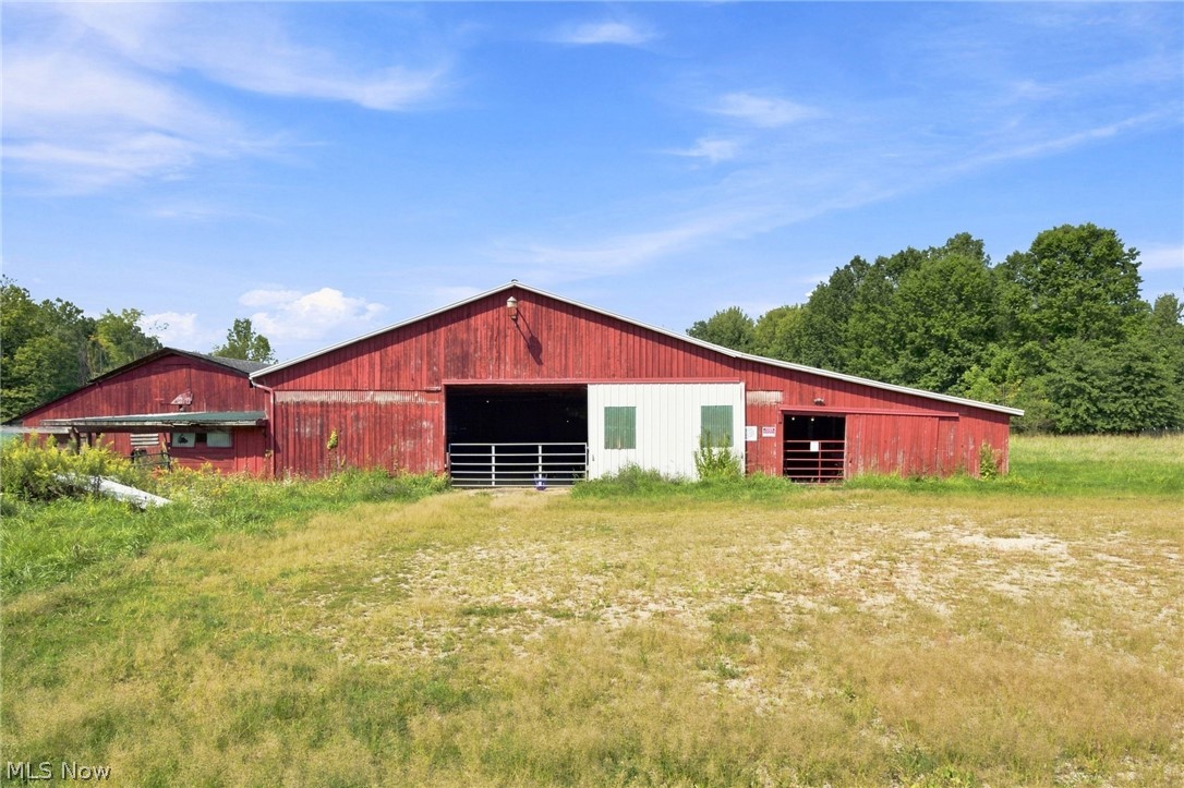Red barn with open bays and white sliding doors beside a grassy field.