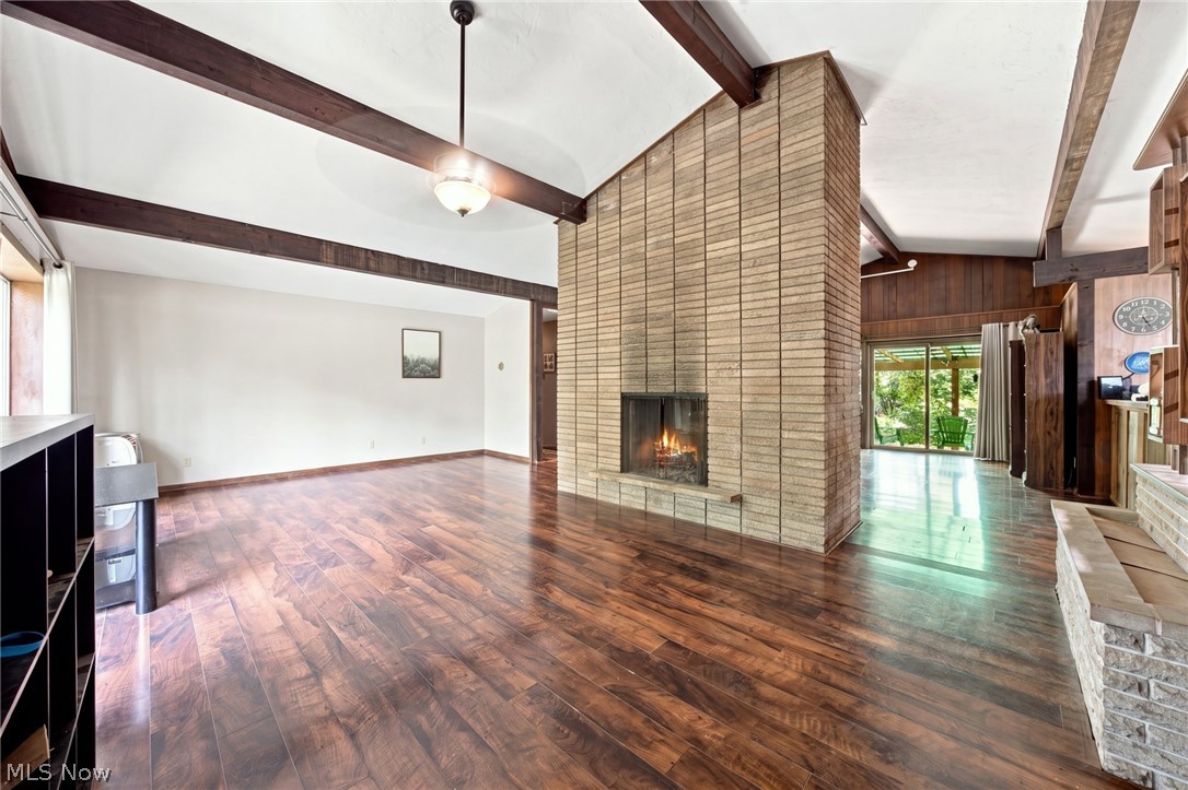 Open living room with a tall brick fireplace, exposed beams, and hardwood floors.