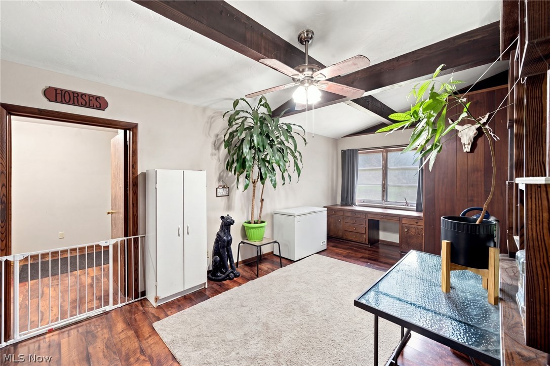 Furnished room with exposed ceiling beams, a window desk, dark wood floors, and potted plants.