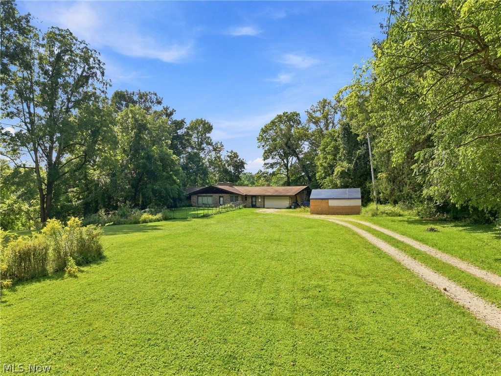 Single-story house at the end of a gravel driveway, surrounded by a broad lawn and mature trees.