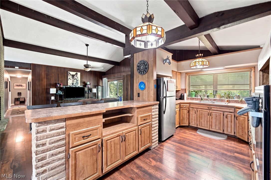 Open kitchen with a stone-sided island, wood cabinetry, stainless steel appliances, and exposed ceiling beams.