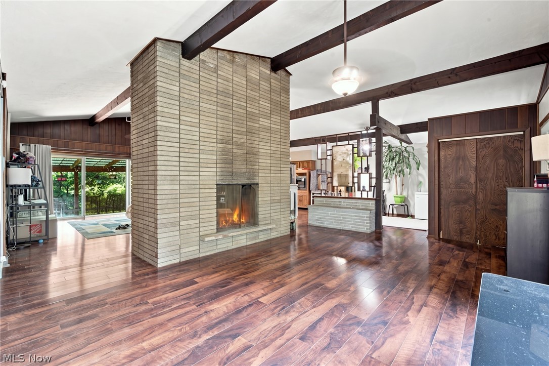 Open-plan living room with a tall brick fireplace, exposed beams, and polished wood floors.