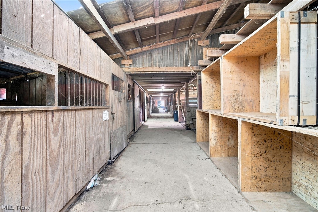Barn aisle with exposed roof beams, wooden stall openings, and large plywood compartments.