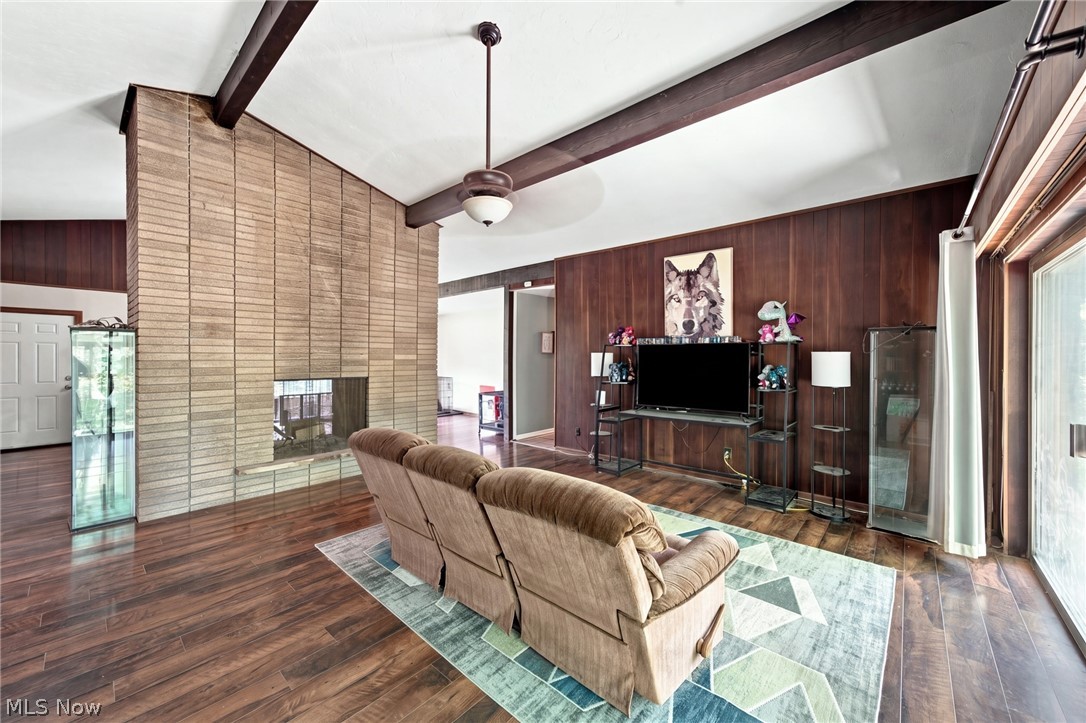 Living room with a tall brick fireplace, exposed ceiling beams, and dark wood-paneled walls.