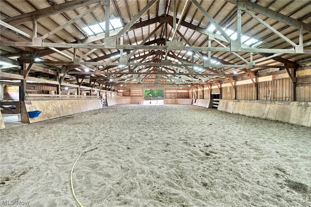 Indoor riding arena with a sandy floor, exposed timber trusses, skylights, and wooden walls.