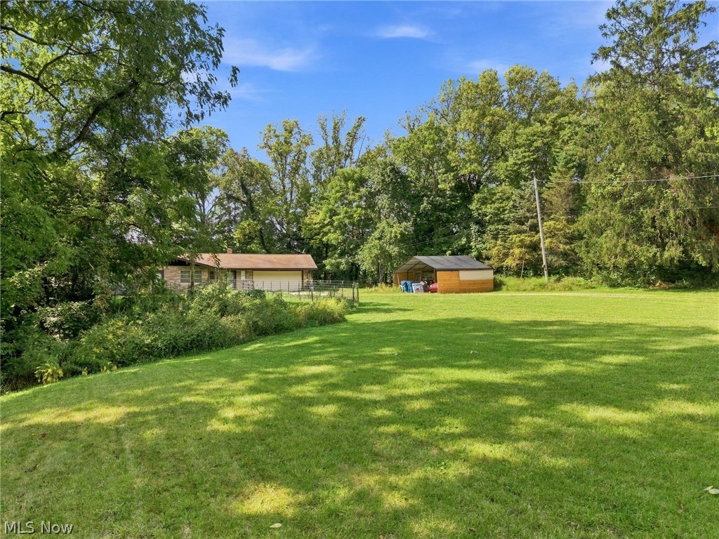 House and detached shed beyond a broad lawn, framed by mature trees.
