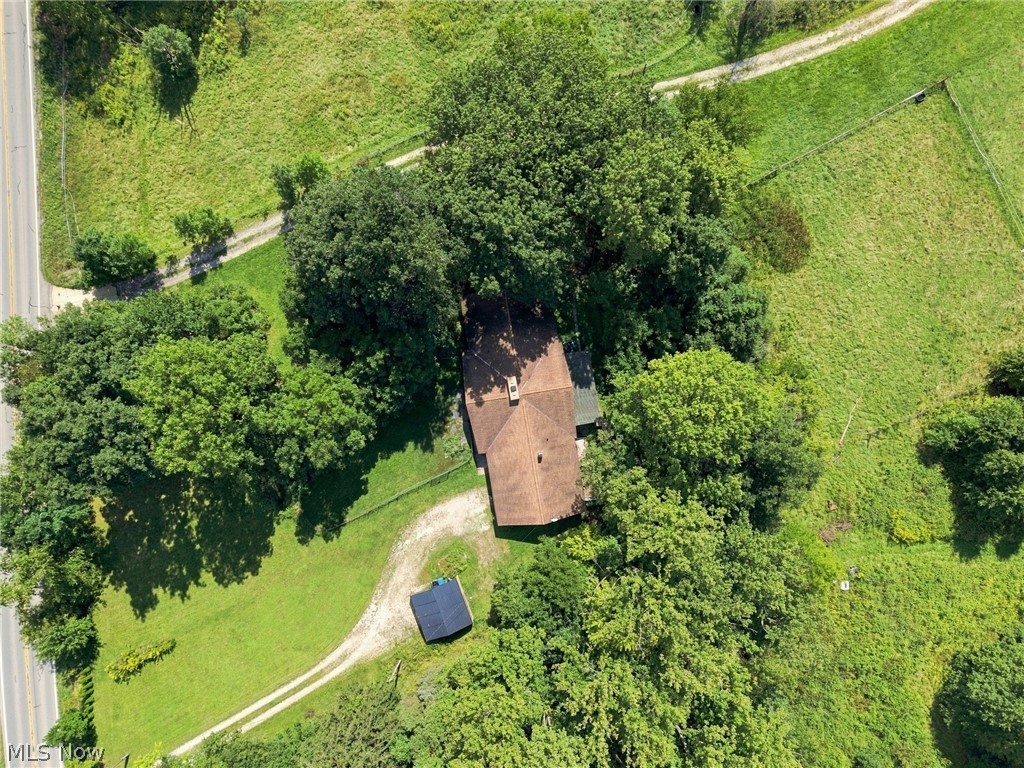 Aerial view of a tree-surrounded house with a curved gravel driveway and solar-paneled outbuilding.