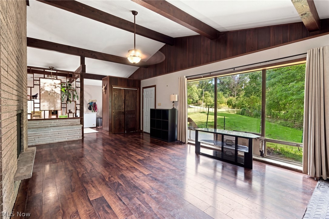 Living room with dark wood floors, exposed beams, a stone fireplace, and sliding doors overlooking a green yard.