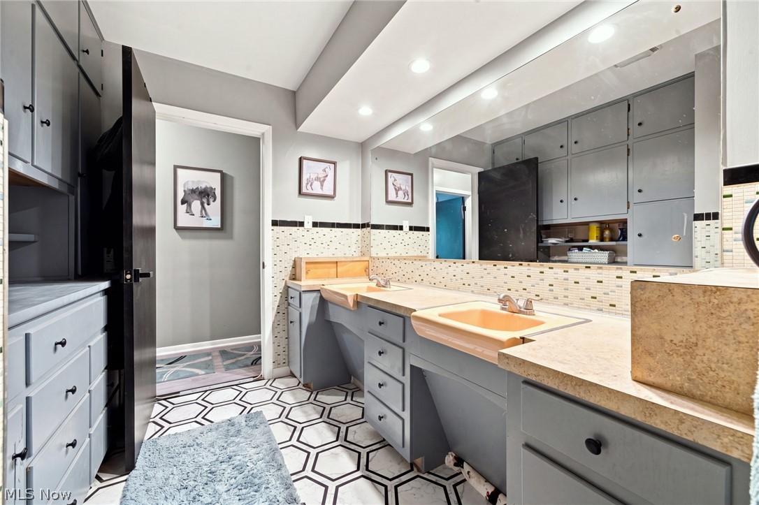 Bathroom with a gray double-sink vanity, peach basins, mosaic backsplash, and geometric tile floor.