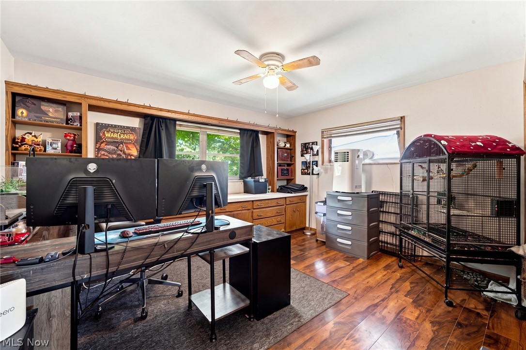 Home office with dual monitors, built-in wood shelving, and a large bird cage.
