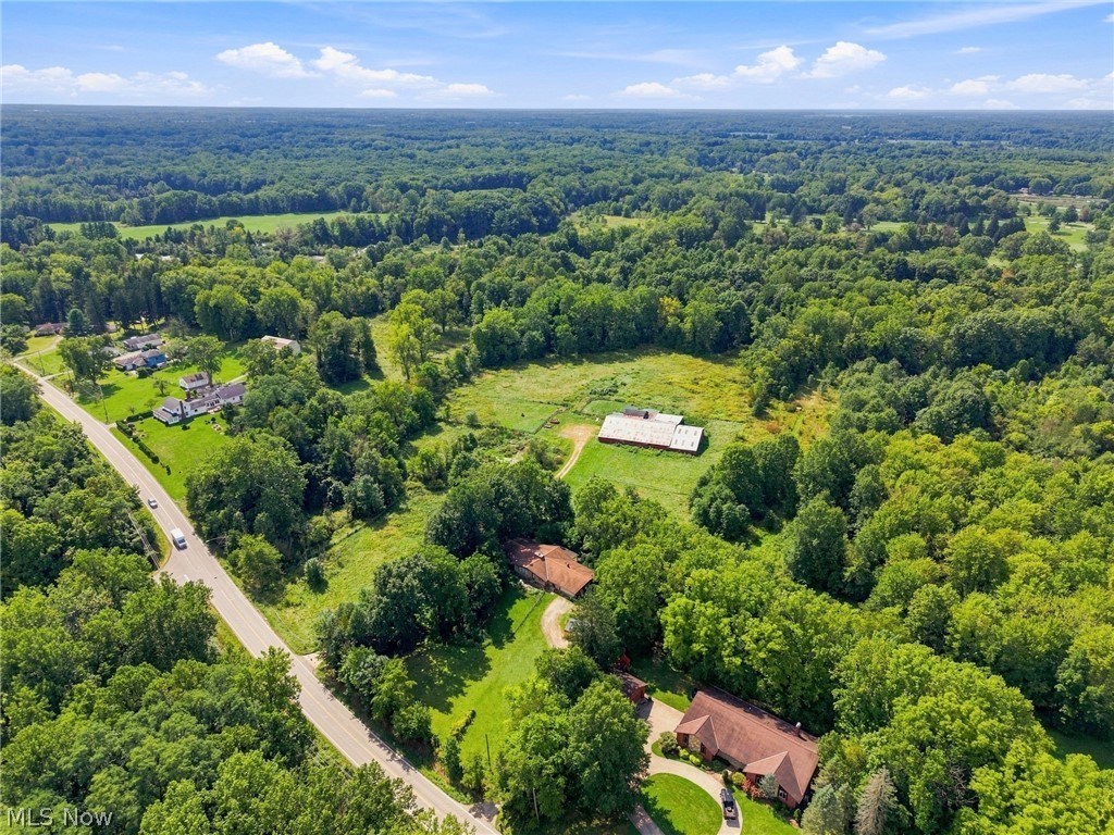 Aerial view of a wooded property with fields, outbuildings, and a road.