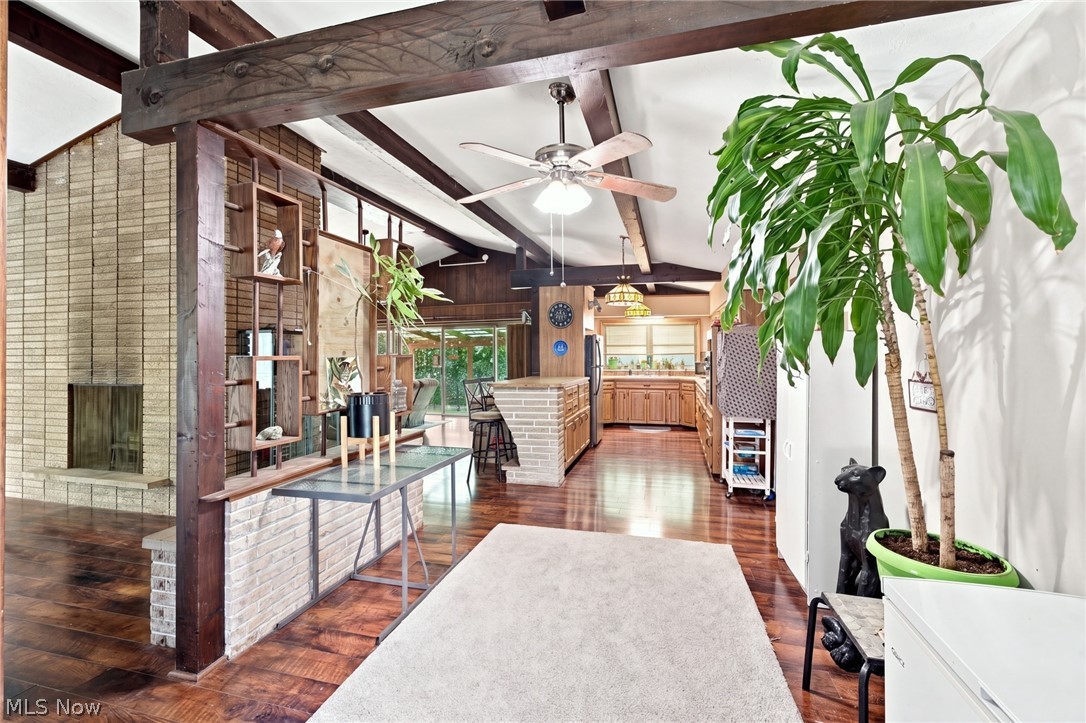 Open-concept living room with a stone fireplace, exposed beams, and a view into the kitchen.