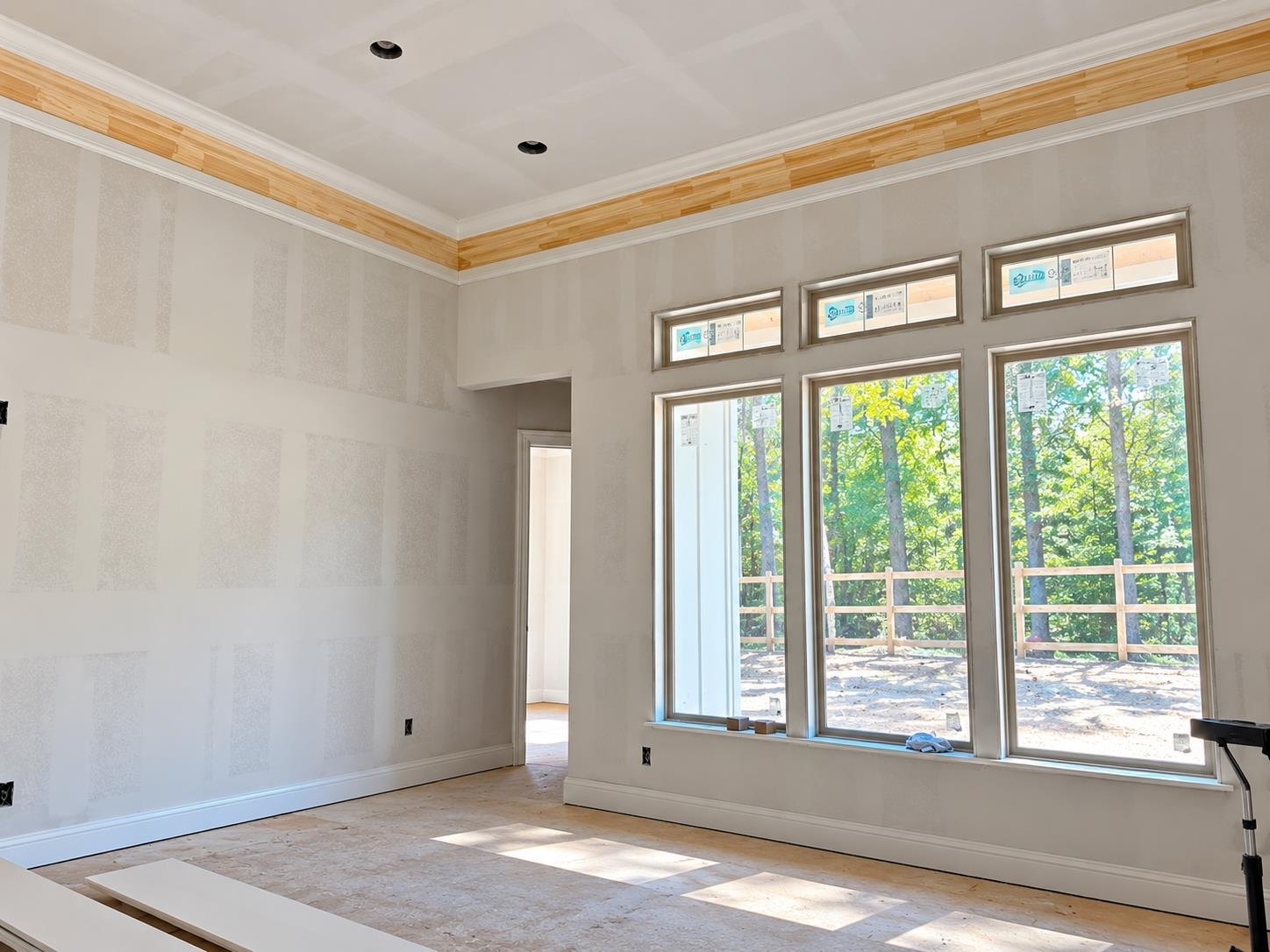 Unfinished room with tall windows overlooking trees and a wooden fence.