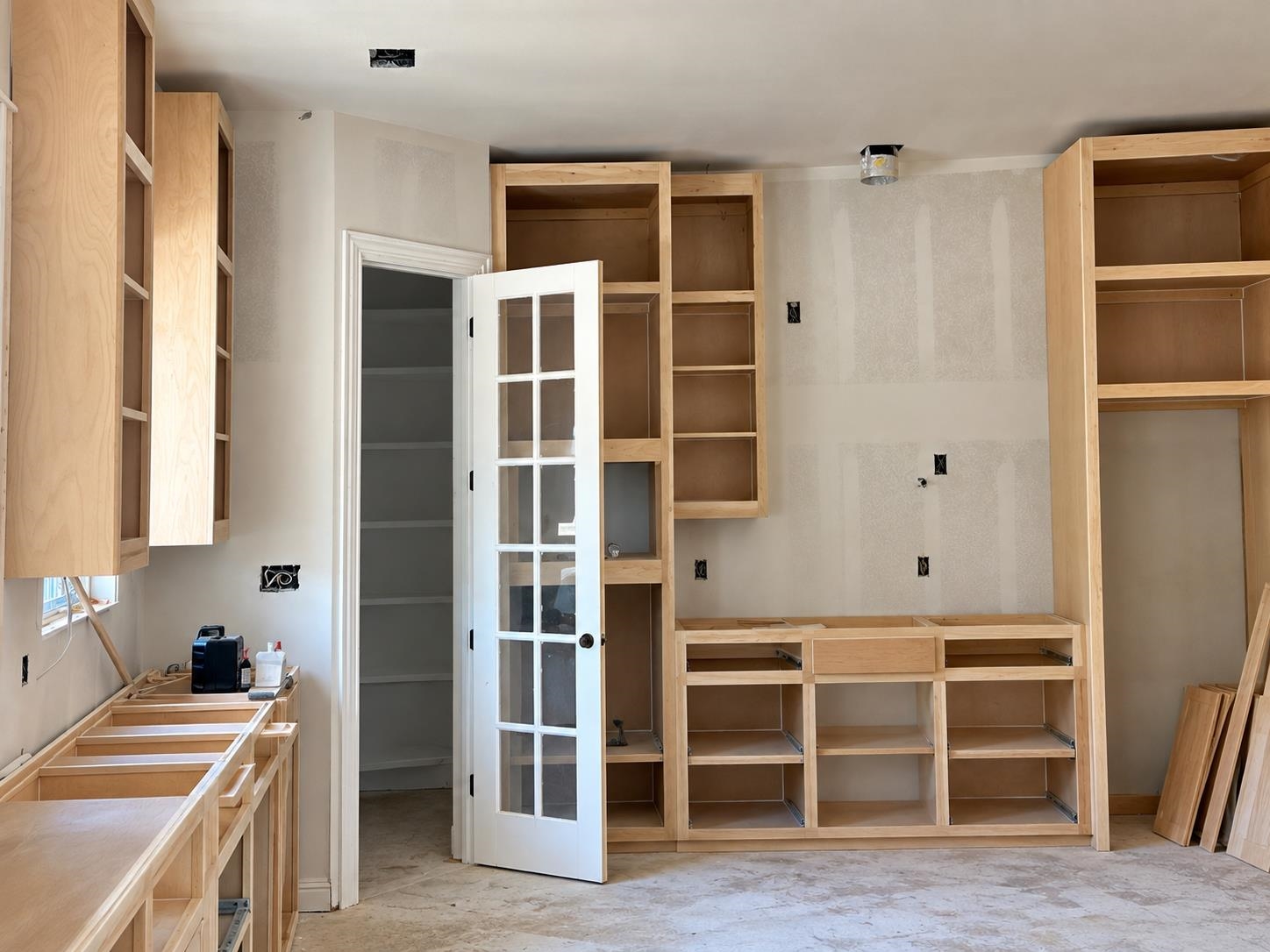 Unfinished room with light-wood built-in cabinets and an open glass-paneled door.