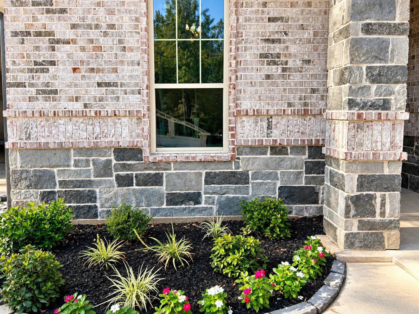 Stone-and-brick home exterior with a tall window and curved flower bed.