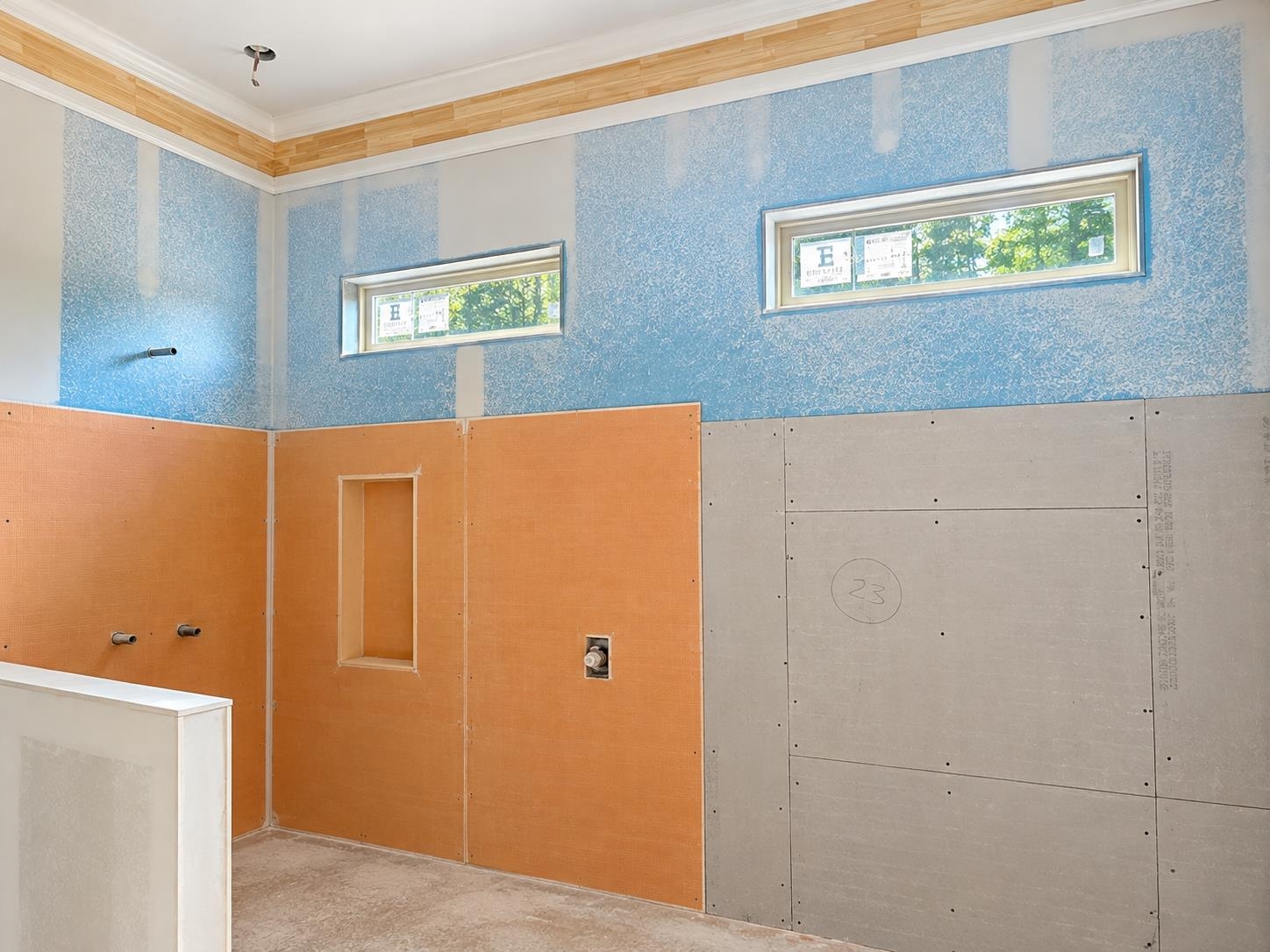 Bathroom under construction with blue patterned walls, high narrow windows, and unfinished shower panels.