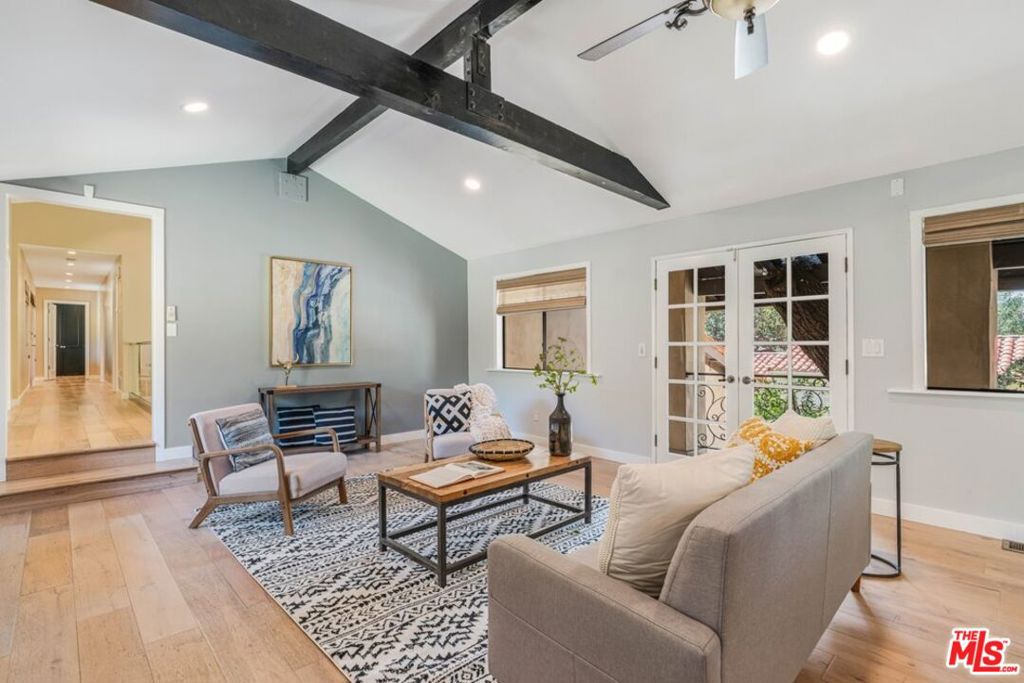 Living room with vaulted ceiling, exposed dark beams, French doors, and neutral furnishings.