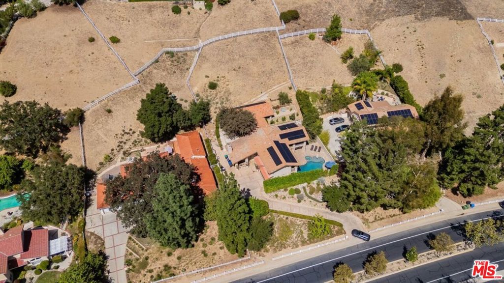Aerial view of a sprawling home with solar panels, swimming pool, and fenced dry grounds.