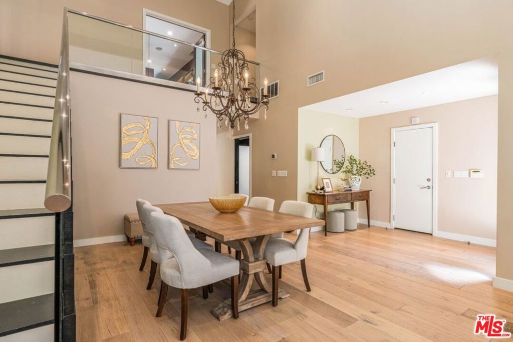 Dining room with a long wood table, upholstered chairs, and a chandelier beneath a mezzanine.