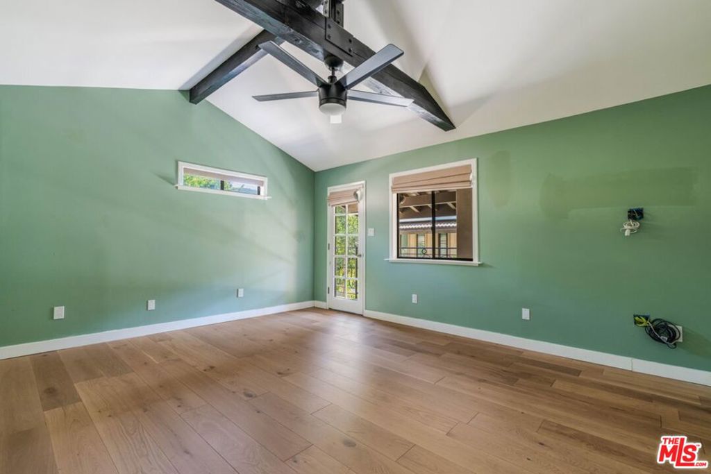 Empty room with green walls, vaulted ceiling, exposed beams, and light wood flooring.