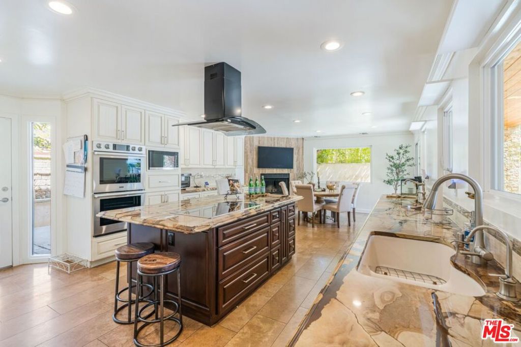 Kitchen with a dark central island, marble countertops, and built-in stainless steel appliances.
