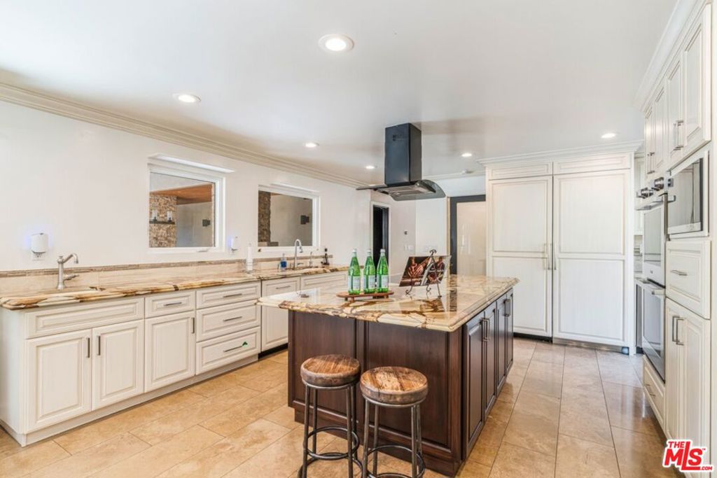 Kitchen with a marble island, two stools, white cabinetry, and stainless steel appliances.