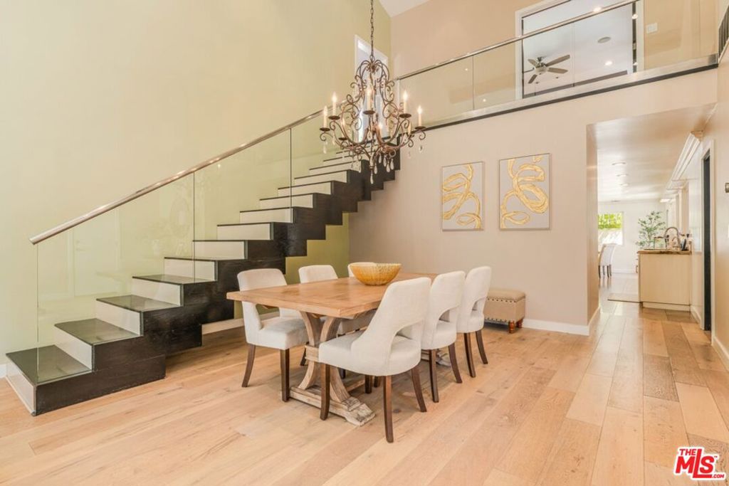 Dining room with a wood table beneath a chandelier beside a glass-railed staircase.