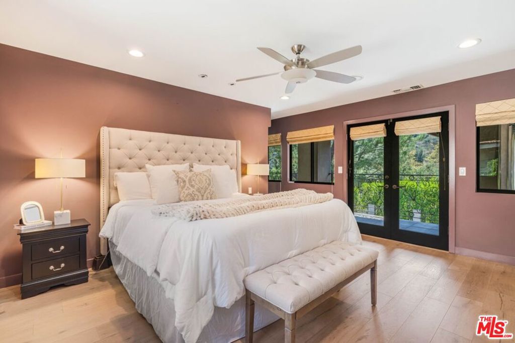 Bedroom with a tufted upholstered bed, mauve walls, and black-framed doors opening to greenery.
