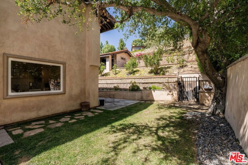 Shaded backyard courtyard with lawn, stepping stones, and terraced retaining walls.