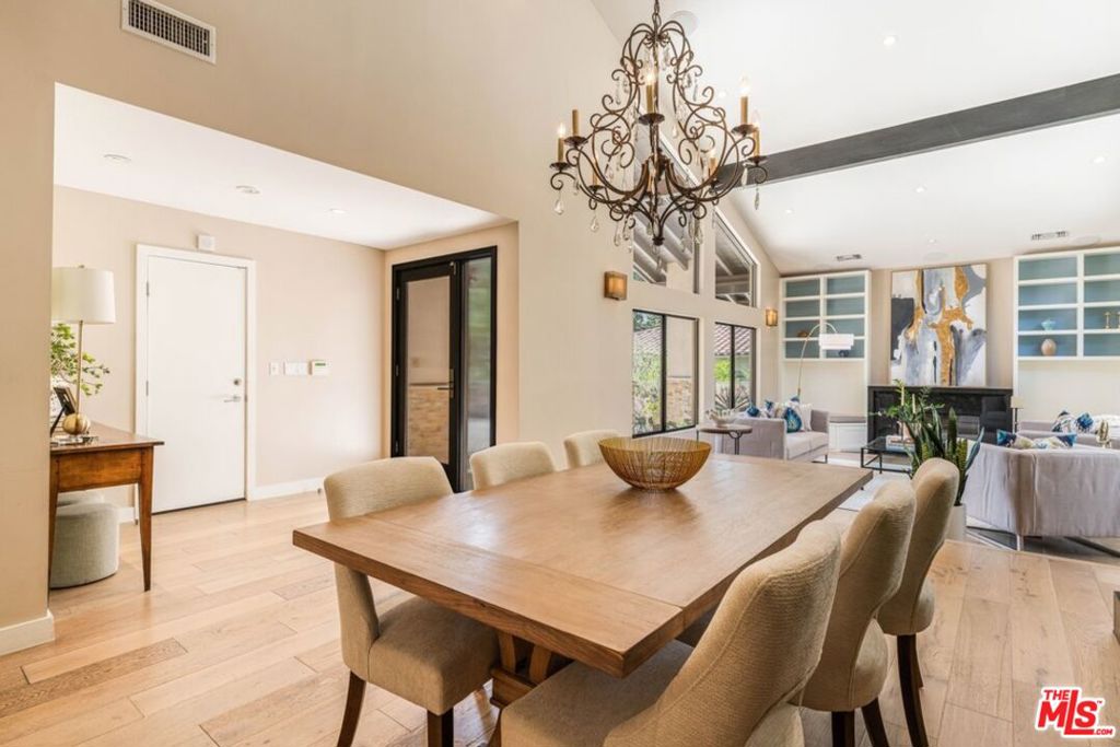 Dining area with a long wooden table beneath an ornate chandelier, opening into a living room.