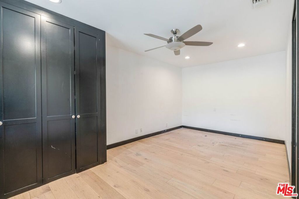 Vacant bedroom with dark built-in closets, light wood flooring, and a ceiling fan.
