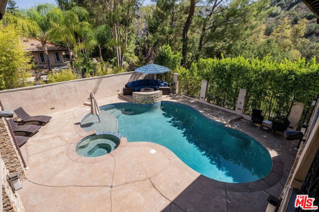 Backyard pool and spa with curved turquoise water, stone fire pit, and shaded seating.
