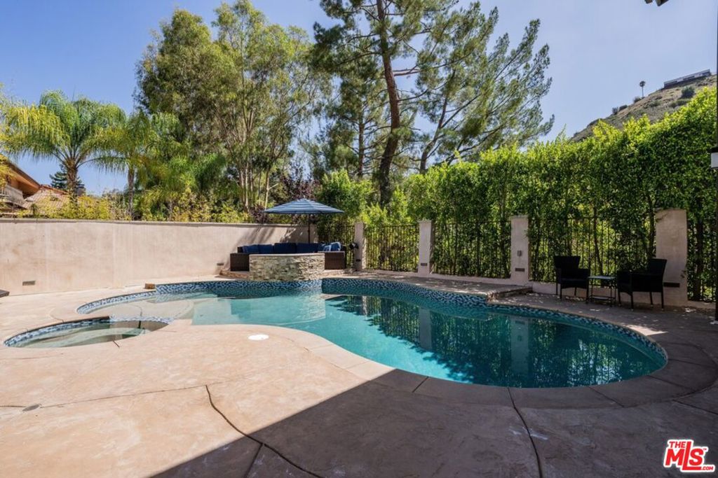 Backyard swimming pool and spa with stone patio, privacy hedges, and outdoor seating.