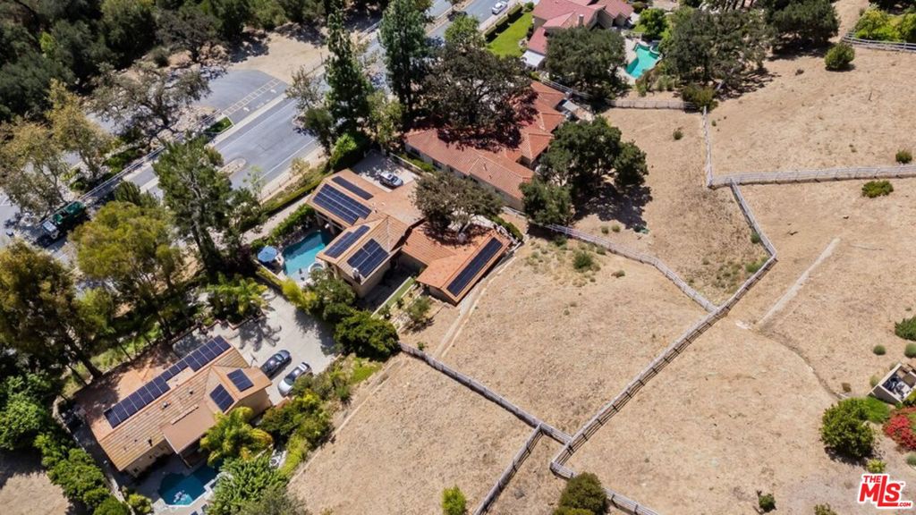 Aerial view of a solar-paneled home with a pool and large fenced lot.