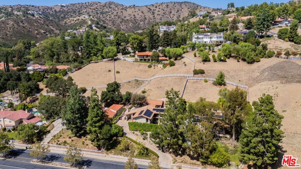 Aerial view of a hillside home surrounded by dry, fenced terrain and neighboring homes.