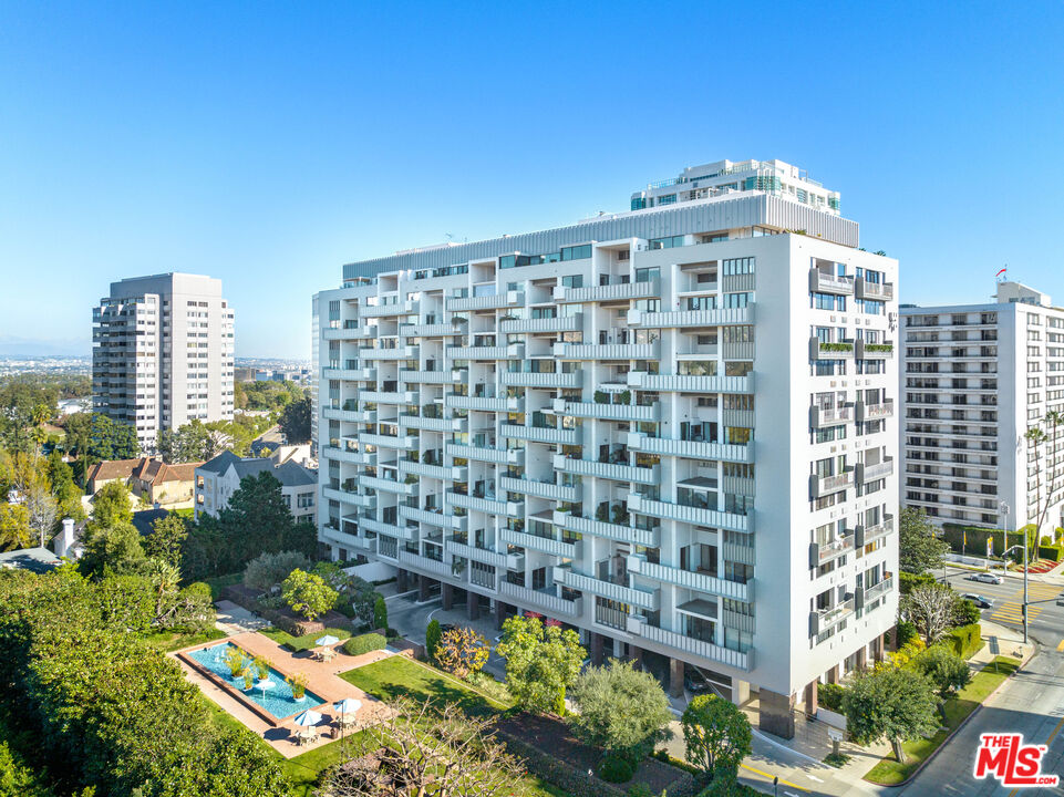 White condominium tower with stacked balconies overlooking a landscaped pool area.