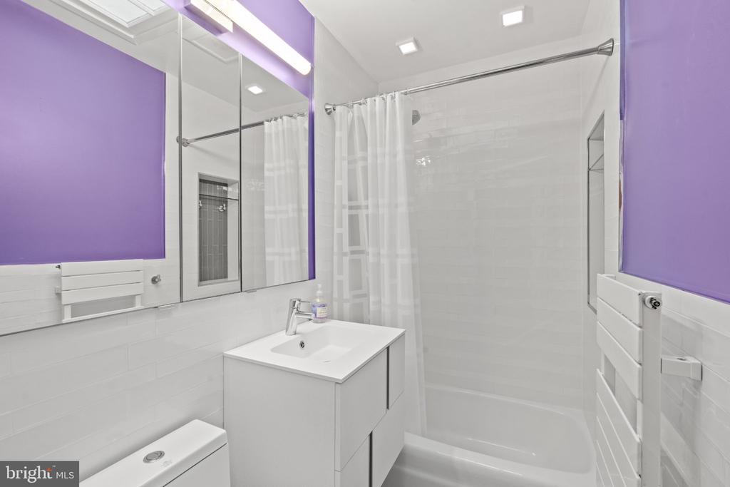 Bathroom with purple walls, white tile, a mirrored cabinet, and a tub-shower with a white curtain.