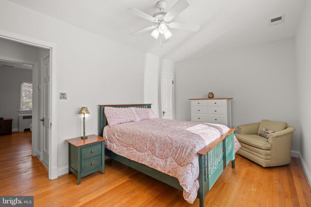 Bedroom with a green bed frame, floral bedding, hardwood floors, and a beige armchair.