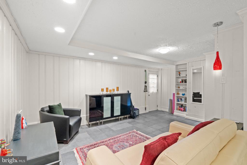 Living room with white paneled walls, gray tile floors, a cream sofa, and built-in shelving.