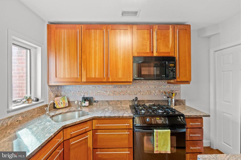 Kitchen with honey-colored cabinets, granite counters, and a black gas range beneath a microwave.