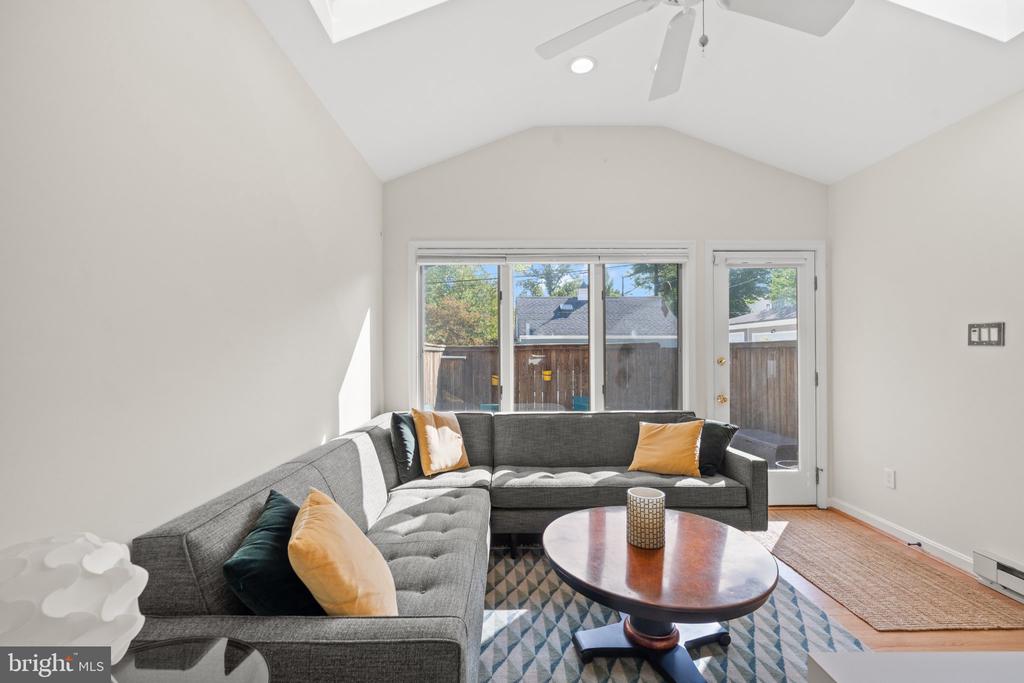 Living room with a gray sectional, patterned rug, and windows overlooking a fenced yard.