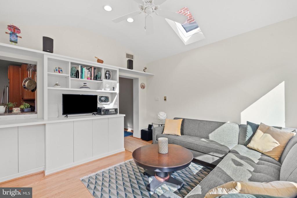 Living room with built-in white shelving, gray sectional sofa, and a skylight above.
