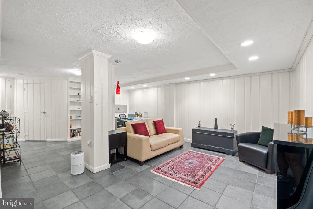 Furnished living room with gray tile floors, a beige sofa, and a red patterned rug.