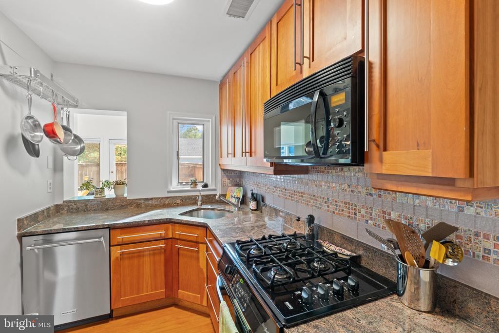 Kitchen with warm wood cabinetry, granite counters, mosaic backsplash, and a gas range.
